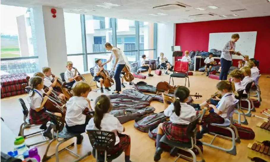 Primary school children seated in a circle with string instruments during a music lesson at Dulwich College Yangon