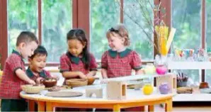 Four pre-school children in red uniforms and aprons working with clay at a round table