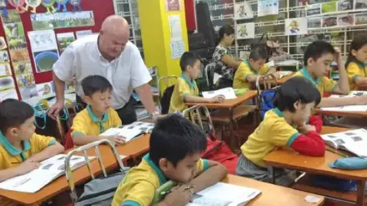A teacher assisting primary school students working at their desks in a classroom